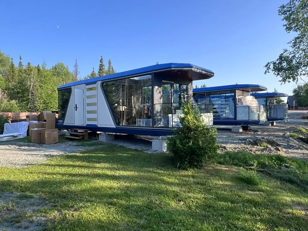 white and blue panoramic prefab capsule cabins installed at a green summer site