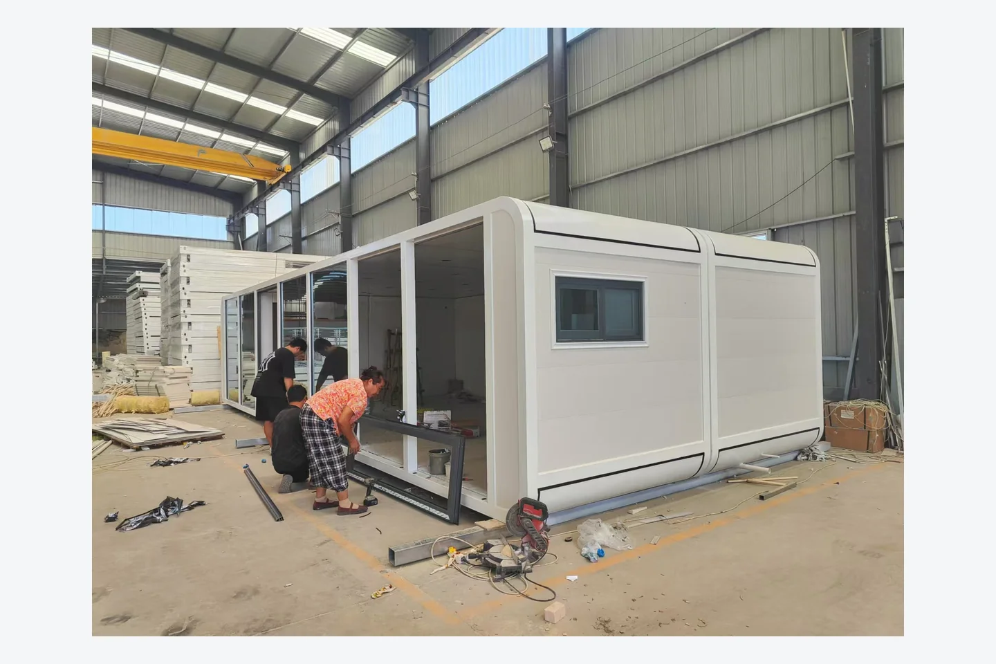 workers installing panoramic glass frames on a 40ft white Apple Cabin in the factory