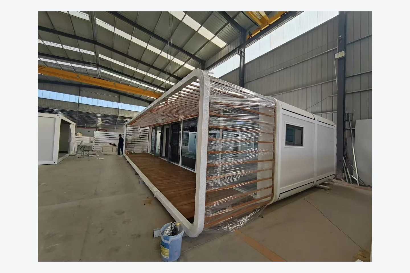40ft white Apple Cabin with full-length covered pergola and wood-look veranda in factory
